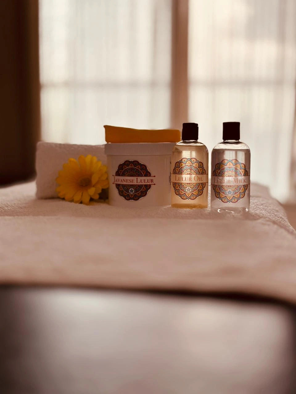 Two bottles and a jar of BORAGE on a towel with a flower, against a blurred window background.